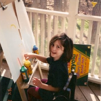 Child painting outdoors on an easel with paints.